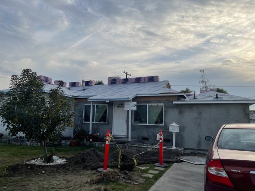 Single-story house with a partially completed roof, surrounded by construction materials.