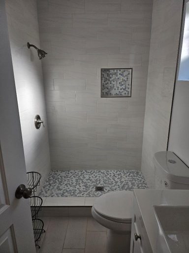 Modern bathroom with a shower area, toilet, and white tile walls.