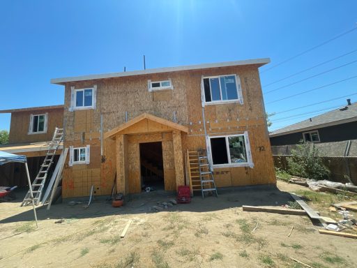 Two-story house under construction, with wooden framing and ladders leaning against the exterior.